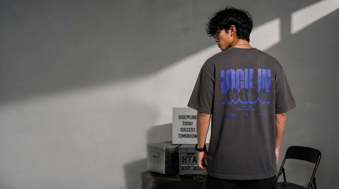 A South Asian man in a charcoal oversized t-shirt standing in a sunlit, minimalist studio space.