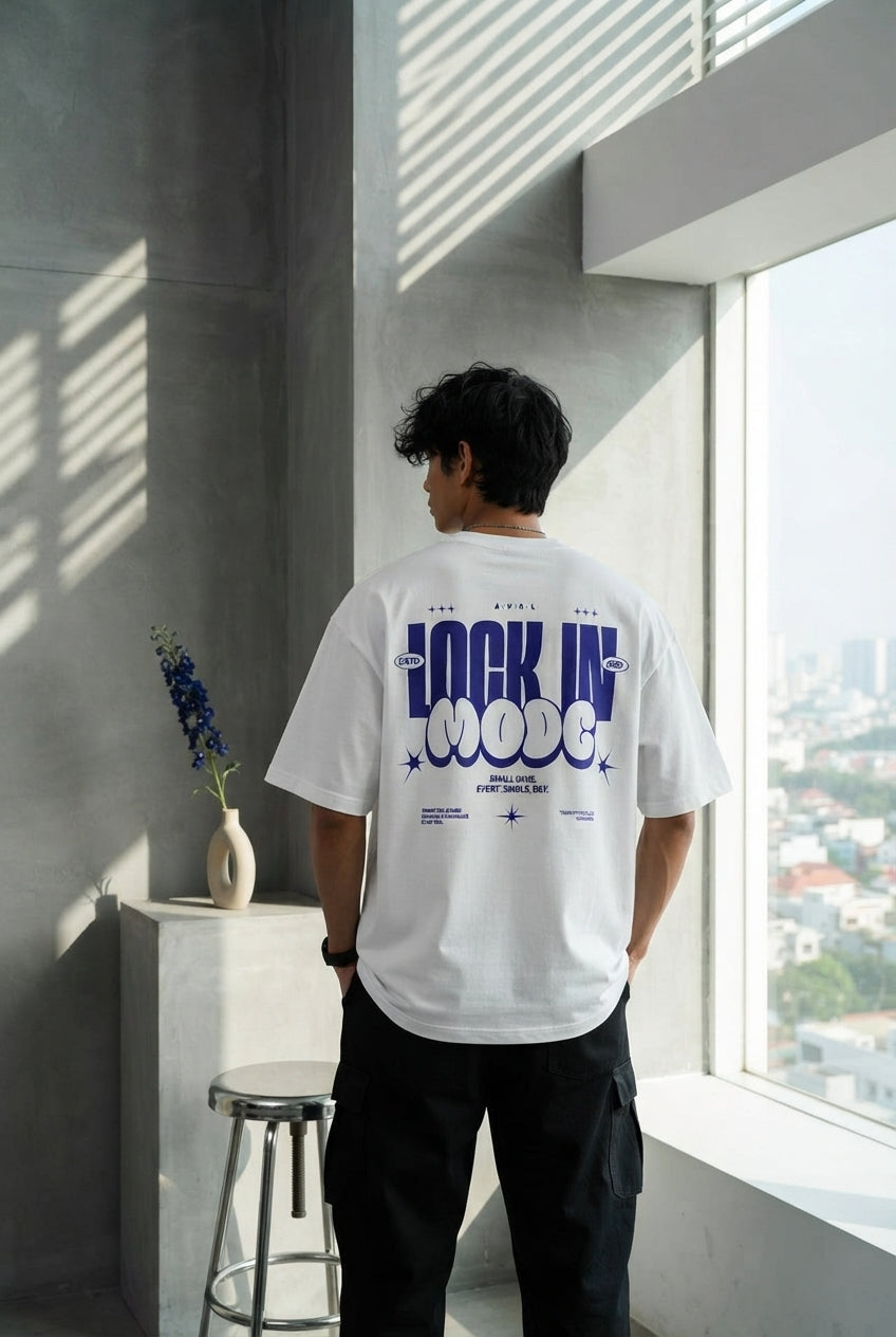 South Asian man in a charcoal oversized t-shirt standing in a minimalist concrete architectural space with bright white accen